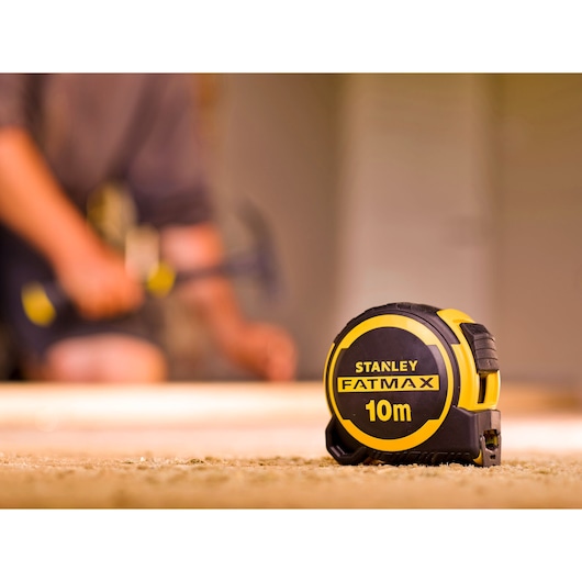 STANLEY FMHT33005-0 FatMax 10m tape measure, yellow and black, shown on workshop floor.