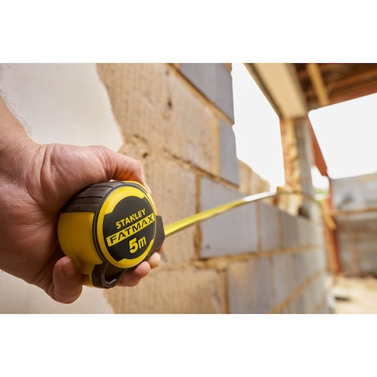 Photo of STANLEY FMHT33100-0 tape measure being used at a construction site, yellow and black design, 5m length.