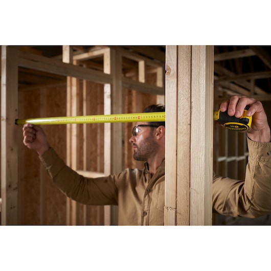 STANLEY FMHT33102-0 tape measure in use measuring wooden framing at a construction site.