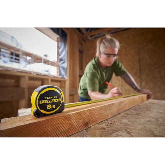 STANLEY FMHT33102-0 tape measure 8m in use, shown on a wooden beam in a construction setting.
