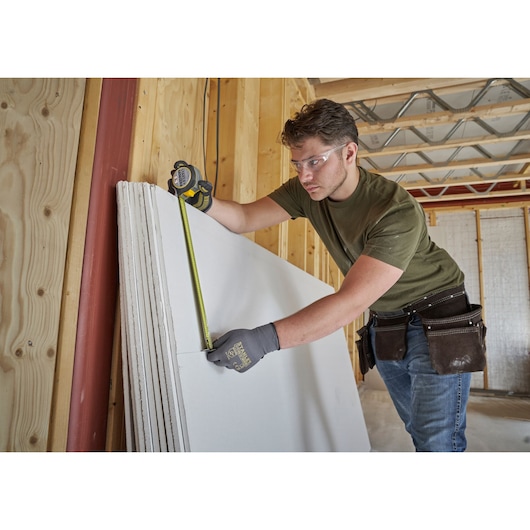 STANLEY FMHT38214-0 tape measure in use measuring drywall panel, construction setting.