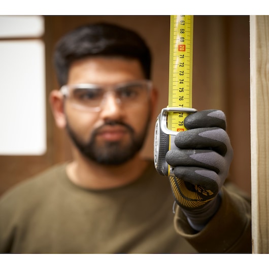 STANLEY FMHT38217-0 tape measure held vertically by gloved hand, close-up, measuring wooden post.