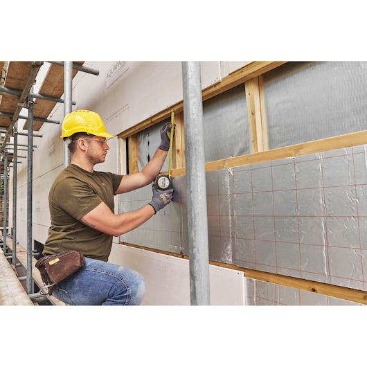 STANLEY FMHT38232-0 tape measure used by a worker measuring a wall frame at a construction site.