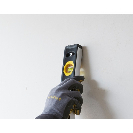 STANLEY FMHT42554-1 spirit level held vertically against a wall by a gloved hand.