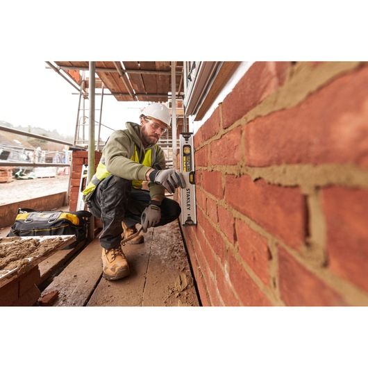 Photo of a worker using a STANLEY FMHT43671-1 spirit level on a brick wall at a construction site.
