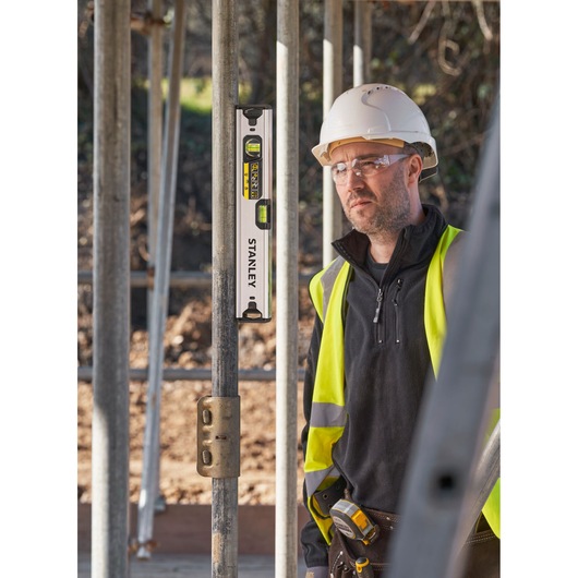 Photo of STANLEY FMHT43671-1 spirit level on metal scaffolding, construction worker in safety gear in background.