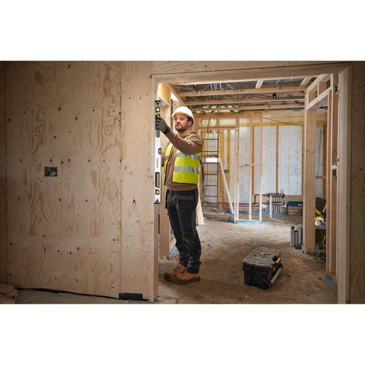 Photo of worker using STANLEY FMHT43674-1 spirit level on wooden door frame at construction site.