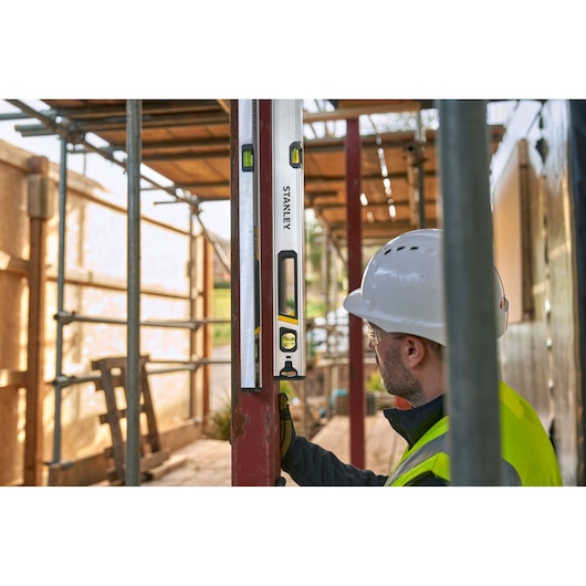 STANLEY FMHT43675-1 spirit level used by worker on construction site, shown vertically against metal beam.