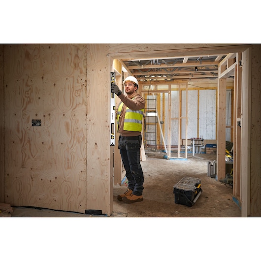 STANLEY FMHT43675-1 spirit level used by worker on wooden door frame at construction site.