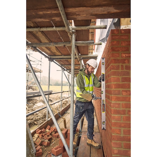 STANLEY FMHT43676-1 spirit level used by a construction worker to check a brick wall on scaffolding.