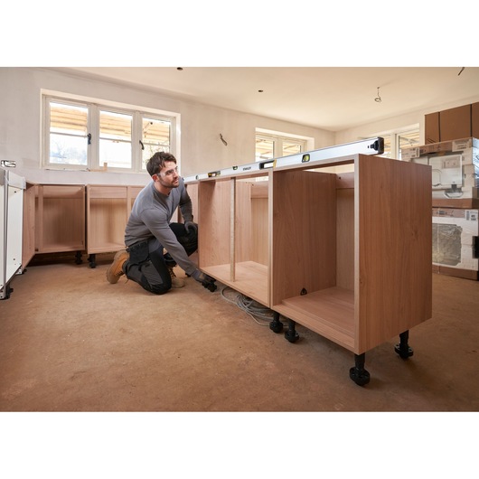 Photo of STANLEY FMHT43679-1 spirit level on wooden kitchen cabinets during installation, with installer adjusting base.