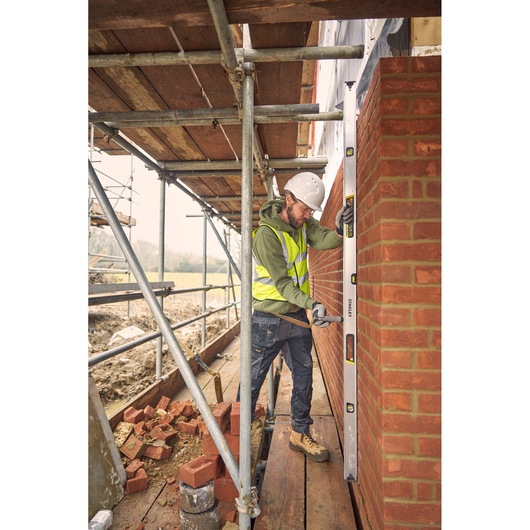 STANLEY FMHT43680-1 spirit level used by a construction worker checking a brick wall's alignment on scaffolding.