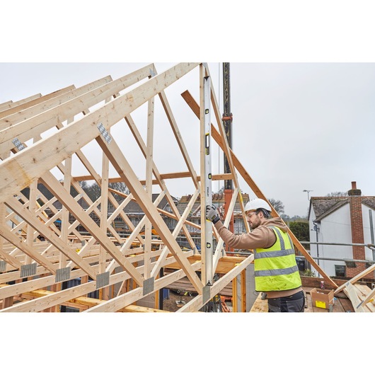 STANLEY FMHT43680-1 spirit level used by worker measuring wooden roof frames at construction site.