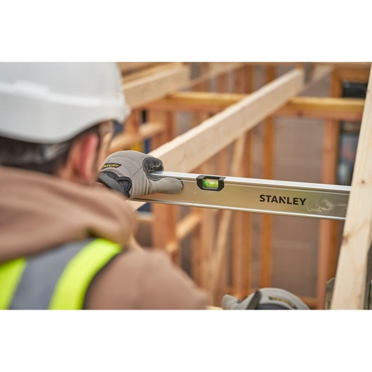 Photo of STANLEY FMHT43680-1 spirit level used by worker at construction site, clear side angle view.