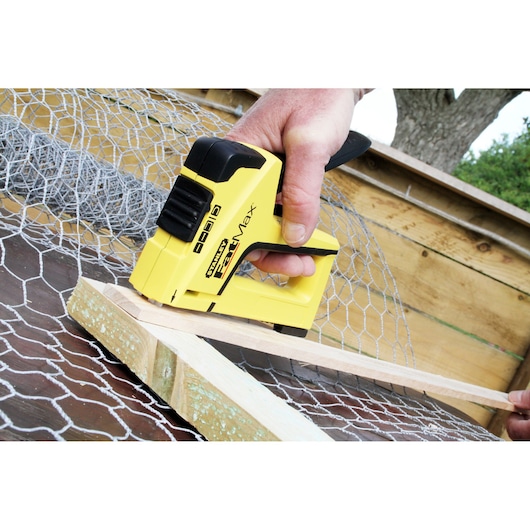 STANLEY FMHT6-70411 yellow hand stapler securing wire mesh to wood, side angle, outdoor setting.