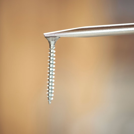Close-up of a screwdriver tip engaging a metal screw against a blurred background.