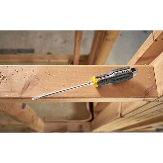 Stanley flathead screwdriver with black and yellow handle lying on a wooden beam in a workshop.