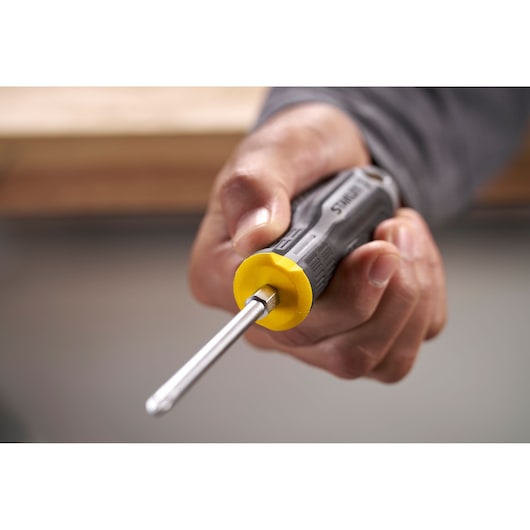 Hand holding a Stanley screwdriver with a yellow and black handle, focusing on the tool tip.