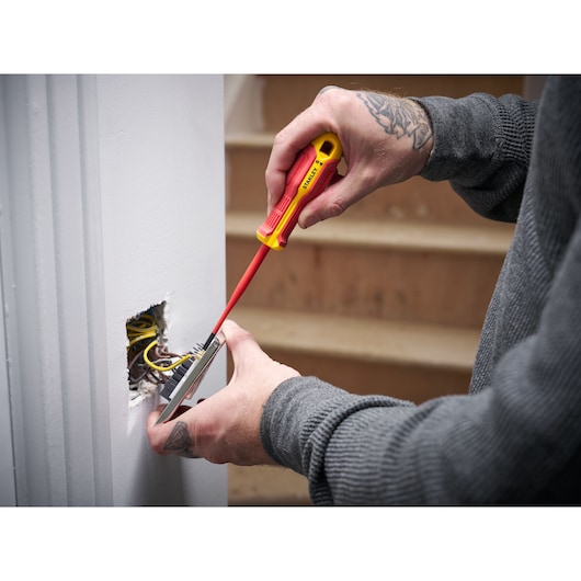 Person uses STANLEY insulated screwdriver to work on electrical wiring in a wall near stairs.