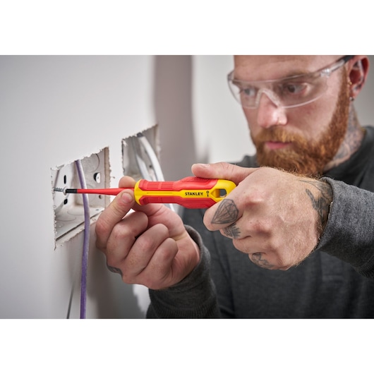 Person uses a STANLEY insulated screwdriver to install a screw in a wall electrical outlet.