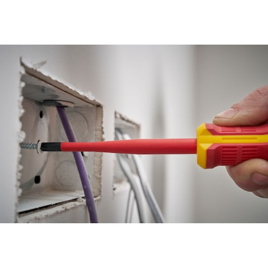 Insulated screwdriver used for electrical work near wires in a wall.