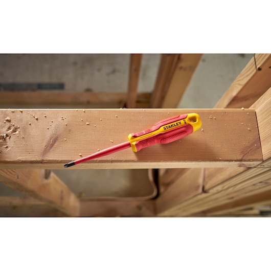 Stanley insulated screwdriver with red and yellow handle resting on wooden beam at construction site.