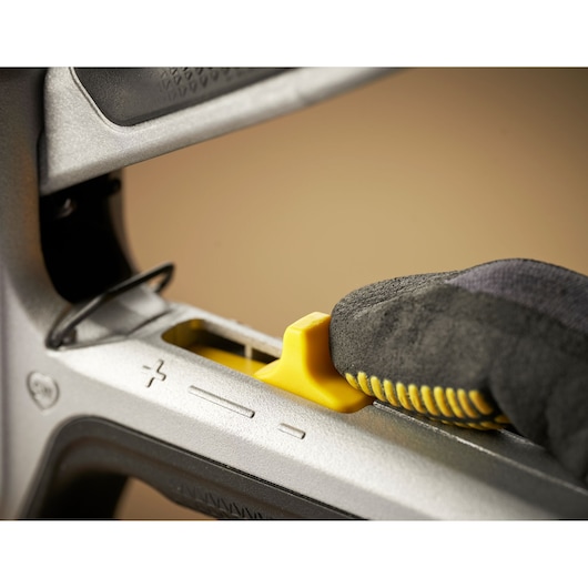 STANLEY FMHT70100-0 staple gun close-up, glove adjusting yellow pressure setting slider.