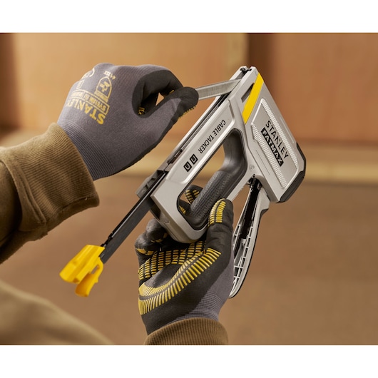 Photo of STANLEY FMHT70100-0 cable tacker tool being loaded with staples, held by gloved hands.