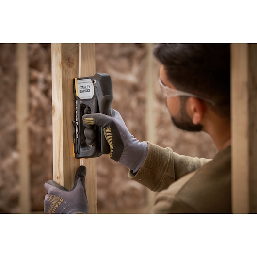 STANLEY FMHT70401-0 stapler used by gloved hands to secure wire to wood frame.