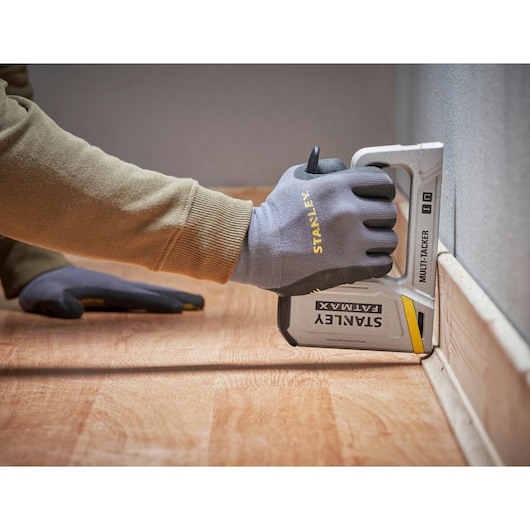 Photo of a gloved hand using a STANLEY FATMAX FMHT70443-0 multi-tacker stapler on flooring next to a wall.