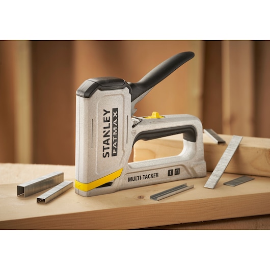 STANLEY FMHT70443-0 manual multi-tacker on wood, with assorted staples, angled indoor photography.