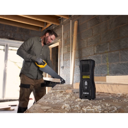 Photo of STANLEY FMHT77165-0 laser measurer on workbench with sawdust, in construction setting.