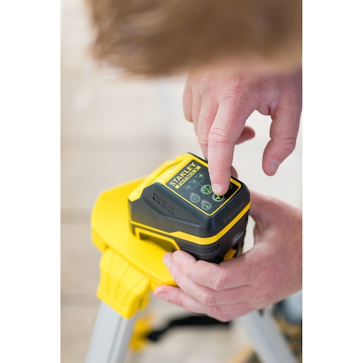 STANLEY FMHT77586-1 laser level on tripod, user pressing control panel, close-up view.