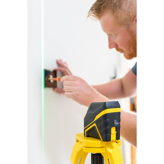 Photo of STANLEY FMHT77586-1 laser level on tripod projecting green line while person fixes wall fitting.