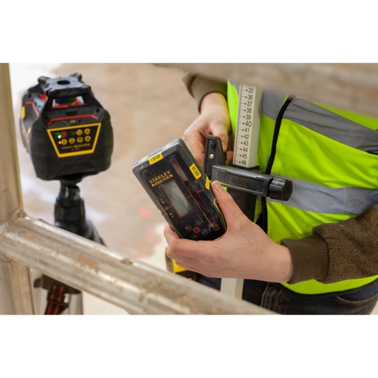 Photo of STANLEY FMHT77652-0 laser detector held in hand, with laser level device in background, construction setting.