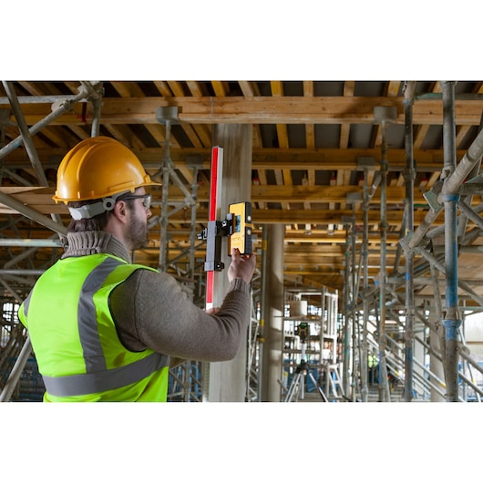 STANLEY FMHT77653-0 laser receiver in use at construction site, held by worker with safety vest and helmet.