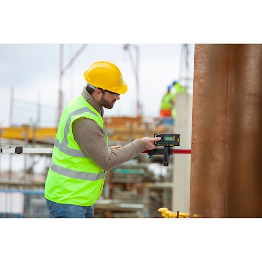 STANLEY FMHT77653-0 laser detector held by worker in high-vis vest and helmet at construction site.