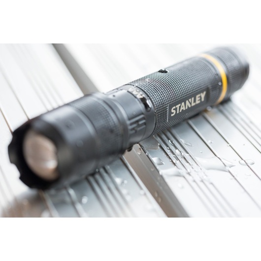 STANLEY FMHT81511-0 black flashlight with textured grip and yellow ring, close-up with water droplets.