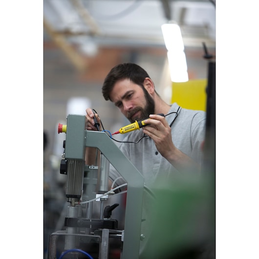 Photo of STANLEY FMHT82566-0 voltage tester in use, worker checking machine wiring in industrial setting.