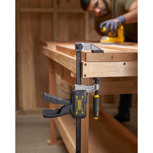 STANLEY FMHT83006-0 bar clamp with yellow and black handle on wooden workbench, side angle photography.