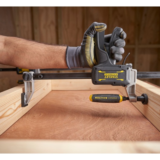 STANLEY FMHT83006-0 clamp tool held by gloved hand, woodworking setup, side angle.