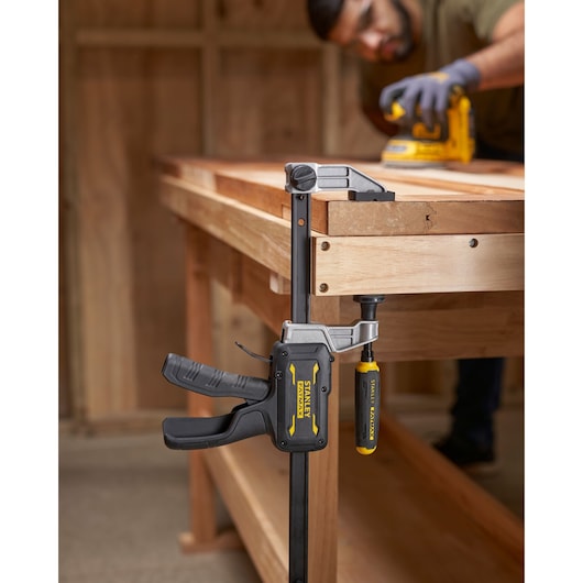 Photo of STANLEY FMHT83007-0 bar clamp attached to a wooden workbench in a workshop setting.