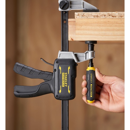 STANLEY FMHT83007-0 clamp in use, black and yellow handle, holding wood, close-up side angle.
