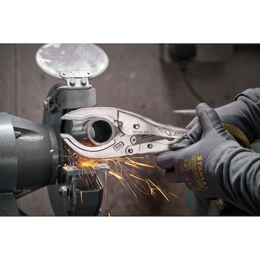 Stanley locking pliers gripping metal pipe as sparks fly from grinder in workshop.
