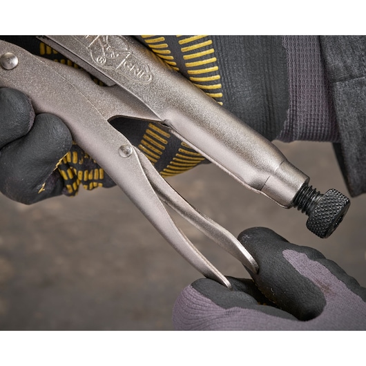 Gloved hand adjusts screw on a metal locking plier tool, focusing on textured grip and adjustment mechanism.