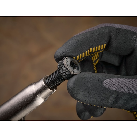 Gloved hand adjusts a STANLEY metal fastener or screw with tool against a blurred brown background.