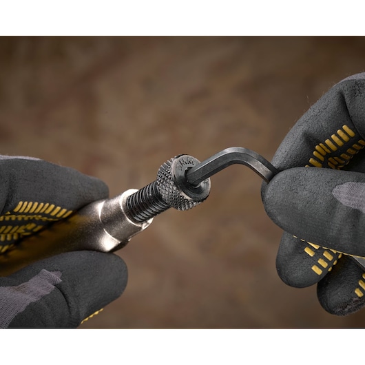 Close-up of gloved hands using an Allen key on a STANLEY tool with a knurled adjustment knob.