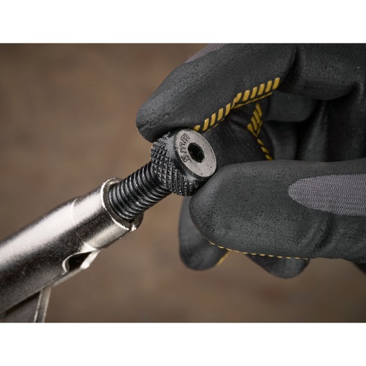 Gloved hand adjusting a metal tool screw with textured grip, branded STANLEY, against a blurred background.