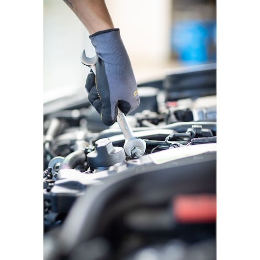 STANLEY FMMT13072-0 wrench used to tighten bolt in car engine, close-up photo, hand with glove.
