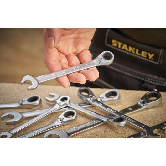 STANLEY FMMT13084-0 ratcheting wrench held in hand, with several wrenches on workbench, photography close-up.